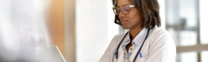 Female doctor working on a laptop in an office, representing healthcare providers addressing the cost of prior authorizations.