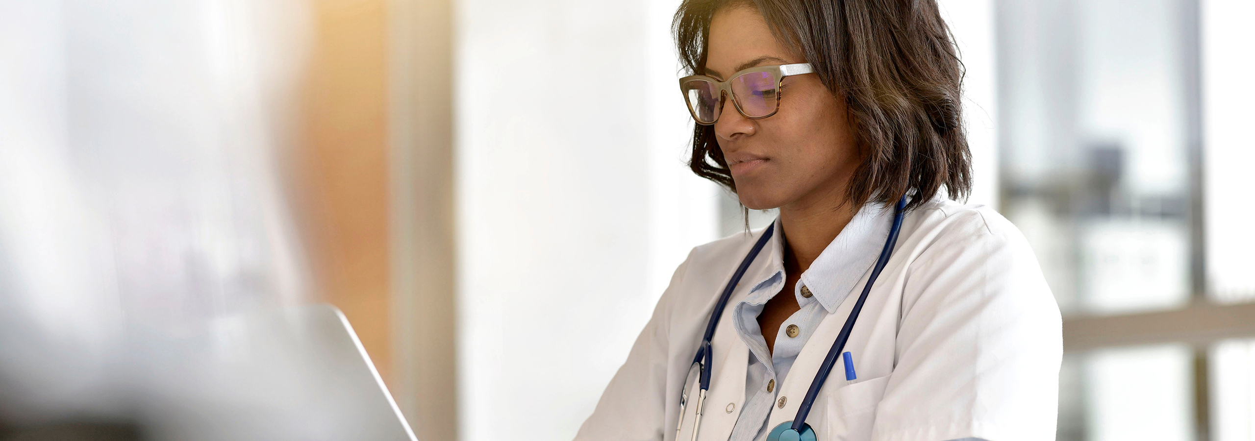Female doctor working on a laptop in an office, representing healthcare providers addressing the cost of prior authorizations.