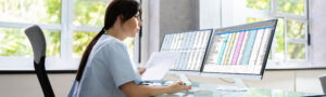 Healthcare professional reviewing spreadsheets on dual monitors, representing medical coding and IDRE claim submission error prevention.