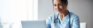 Female physician reviewing clinical documentation on a laptop, representing URAC accreditation and health utilization management in medical reviews.