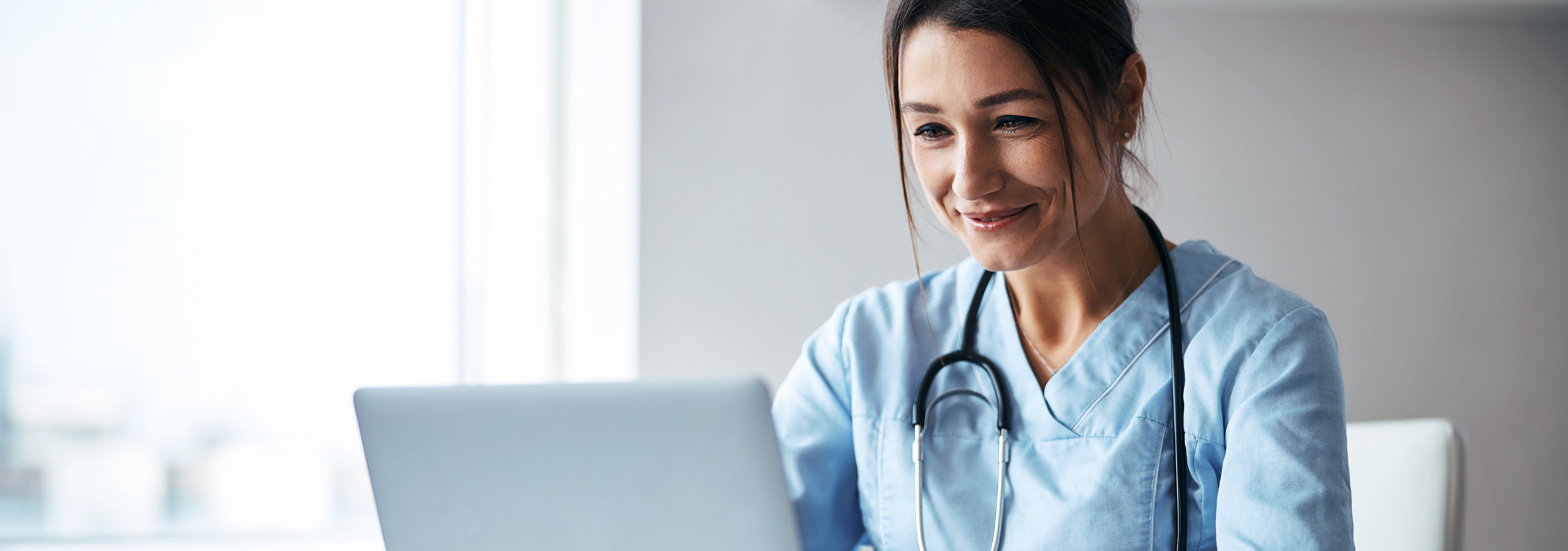 Female physician reviewing clinical documentation on a laptop, representing URAC accreditation and health utilization management in medical reviews.